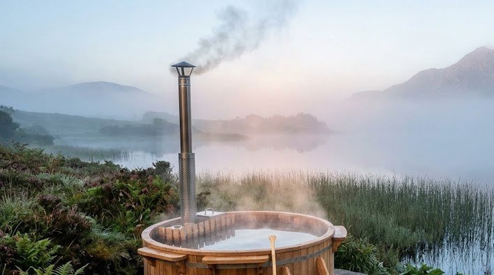 Wood fired hot tub by a lake, the kind of view you get glamping with a hot tub in Ireland